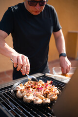A man in sunglasses grilling mushrooms and onions on a barbecue grill, preparing a delicious outdoor mea