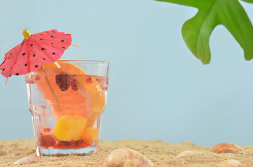 Orange, yellow and red cocktail decorated with little umbrella on beach with shells. Empty space to fill with content. Summertime in exotic place. 