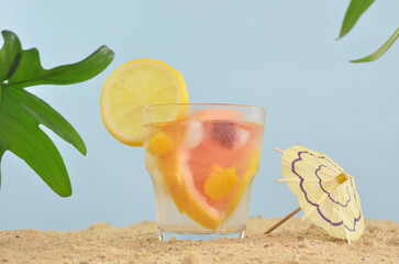 Cold cocktail on the beach with citrus fruits and little umbrella. Blue sky, sand and exotic leaves. 