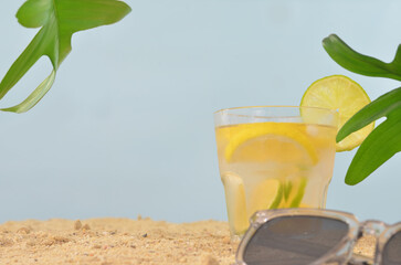 Glass of citrus juice on a beach, blue sky, leaves, sunglasses and empty space to fill with content.