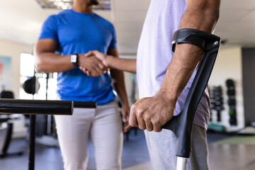Biracial man with crutches shaking hands with male physical therapist