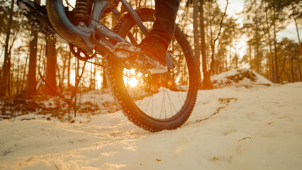 CLOSE UP: Biker doing a wheelie on a snowy trail in amazing golden sunset light