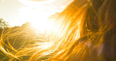 CLOSE UP, LENS FLARE: Gentle summer wind lifting young woman's long wavy hair