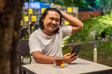 Young Asian man, digital nomad working remotely from cafe, using laptop and smartphone. young Asian...