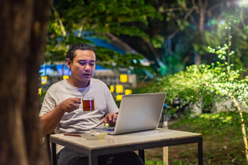 Young Asian man, digital nomad working remotely from cafe, using laptop and smartphone. young Asian...