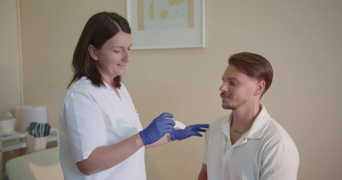 Gorgeous, middle-aged, female doctor measuring young client body temperature using temporal or forehead thermometer.