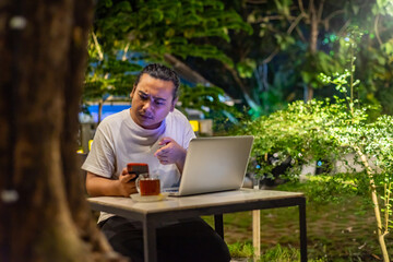 Young Asian man, digital nomad working remotely from cafe, using laptop and smartphone. young Asian...