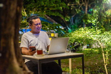 Young Asian man, digital nomad working remotely from cafe, using laptop and smartphone. young Asian...