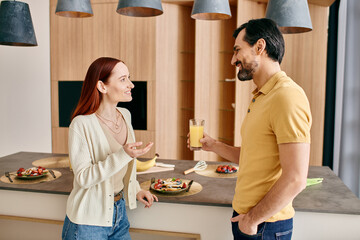 A redhead woman and bearded man talk in a modern kitchen, enjoying quality time together.