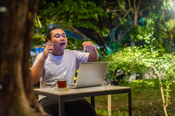 Young Asian man, digital nomad working remotely from cafe, using laptop and smartphone. young Asian...