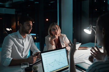 Employee, teamwork and laptop in office at night with documents for deadline or overtime as...