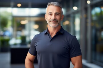 Portrait of a glad man in his 50s donning a classy polo shirt in sophisticated corporate office background