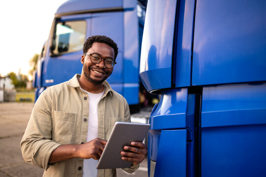 Portrait of smiling driver standing by his truck and holding digital tablet computer.