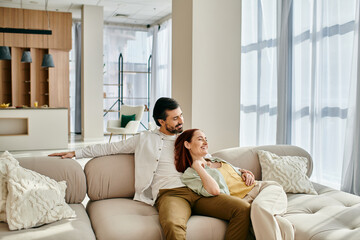 A man and woman, a redhead and a bearded man, relax on a couch in a modern living room, enjoying...