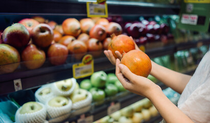 A person selecting pomegranates at a grocery store, with multiple fruits like apples on display. Suitable for promoting healthy eating, grocery stores, autumn, and commercial purposes.
