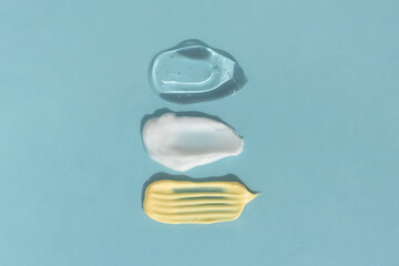 Smears of yellow, white cream and transparent gel or serum on a blue background. The texture of a cosmetic skin care product. Top view.