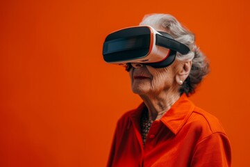 Close-up portrait of senior grey-haired Caucasian woman wearing VR headset on bright orange background. Excited retired lady using futuristic technologies. Active lifestyle for elderly people.
