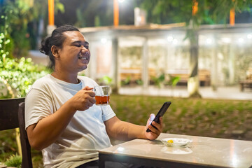 Young Asian man, digital nomad working remotely from cafe, using laptop and smartphone. young Asian men are hanging out in a cafe with a nature theme at night