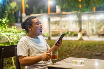 Young Asian man, digital nomad working remotely from cafe, using laptop and smartphone. young Asian...