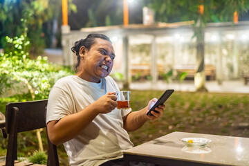 Young Asian man, digital nomad working remotely from cafe, using laptop and smartphone. young Asian men are hanging out in a cafe with a nature theme at night