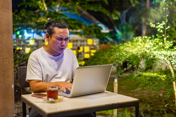 Young Asian man, digital nomad working remotely from cafe, using laptop and smartphone. young Asian...