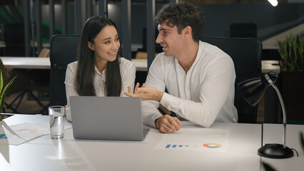Cheerful Caucasian talking smiling laughing with laptop computer pc in office colleagues male manager and female businesswoman at desk working discussing project together having fun corporate business