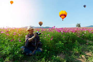 Lifestyle traveler women raise hand feeling good relax and happy freedom and see the fire balloon outdoors the nature tea and cosmos farm in the sunrise morning. Travel and summer Concept