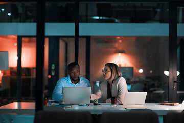 Employee, teamwork and laptop in office at night with documents for deadline or overtime as...