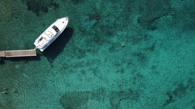 Yacht moored in clear blue Lagoon with few people swimming beside, Drone top down