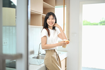 Smiling casual young woman enjoying a hot drink and relaxing in kitchen