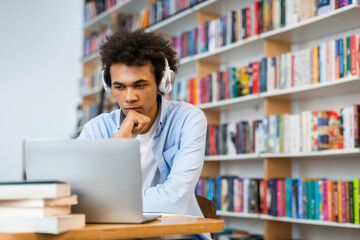 Focused sad latin student guy sitting in front of laptop in university library, poignant scene...