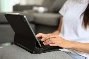 Fototapeta premium Cropped shot young woman using digital tablet sitting on sofa at home