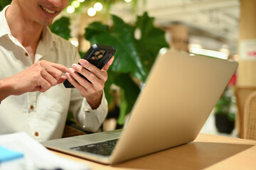 Smiling male office worker using mobile phone while working with laptop at modern coworking space