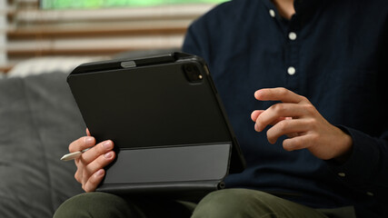 Close up young businessman sitting on sofa at home and using digital tablet