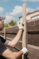 A man builds a wooden fence from boards - rough unedged board for a picket fence