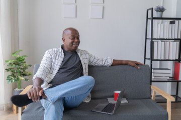 Fototapeta premium Portrait of happy African American small business owner. Millennial black smiling, sitting and using the laptop, and holding a cup of coffee work in modern office.