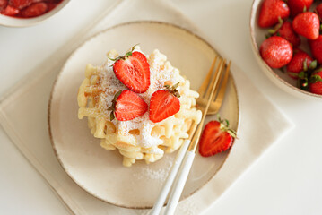 Belgian waffles with strawberries and powdered sugar on white table. Summer food concept. Soft focus