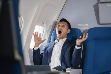 Stressed and anxious businessman sitting on airplane, passengers near window