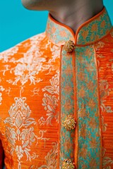 Close-up of a man wearing a vibrant orange traditional embroidered kurta with golden buttons and intricate patterns.