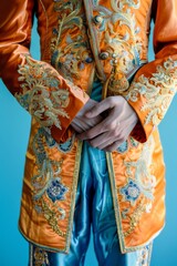 Naklejka premium Close-up of a person wearing an ornate, embroidered orange and blue costume with intricate patterns, holding hands together.