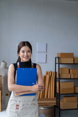 Obraz premium Delivery business. happy modern female in White Shirt checking order with laptop and holding a cup of coffee parcels using smartphone applications in the warehouse