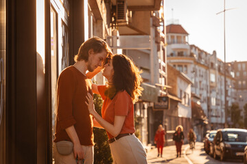 Young couple Caucasian man and woman, are kissing on street. Sunset light city in background