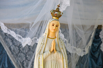 Statue of the virgin mary wearing a crown and praying under a white lace veil
