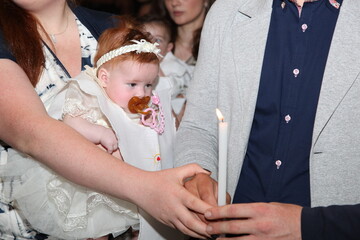 Parents holding a white burning candle with their baby girl during a baptism ceremony in a church