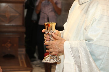 Priest holds a golden chalice in a church ceremony, surrounded by symbols of faith. The atmosphere is spiritual and traditional as he leads worship