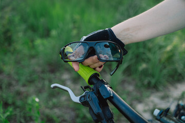 A close up shot of a black mountain bike with a helmet in the foreground, the handlebars in focus, and the cyclist is blurred in the background