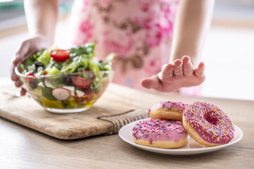Definitely not to sweet temptation. A woman dismissively rejects sweet donuts in front of a healthy vegetable salad