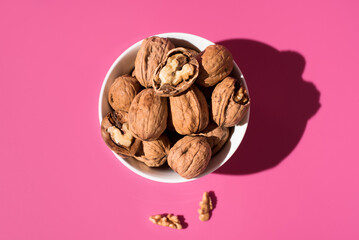 Nueces doradas en un recipiente blanco sobre fondo rosa. Vista superior	