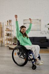Obraz premium A young brunette woman with a disability sits in a wheelchair in her living room and dances along to music playing in her headphones.