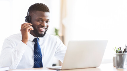 Happy african american consultant with headset looking at laptop, office interior, empty space